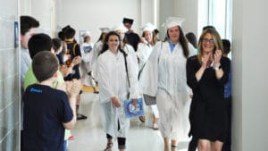 Rockland High School Seniors Macie Jones (middle-left holding blue folder) and Emily McLaughlin walk the halls of the Rogers Middle School 5th grade hallway as Assistant Principal Cheryl Schipper applauds. (Courtesy Photo)