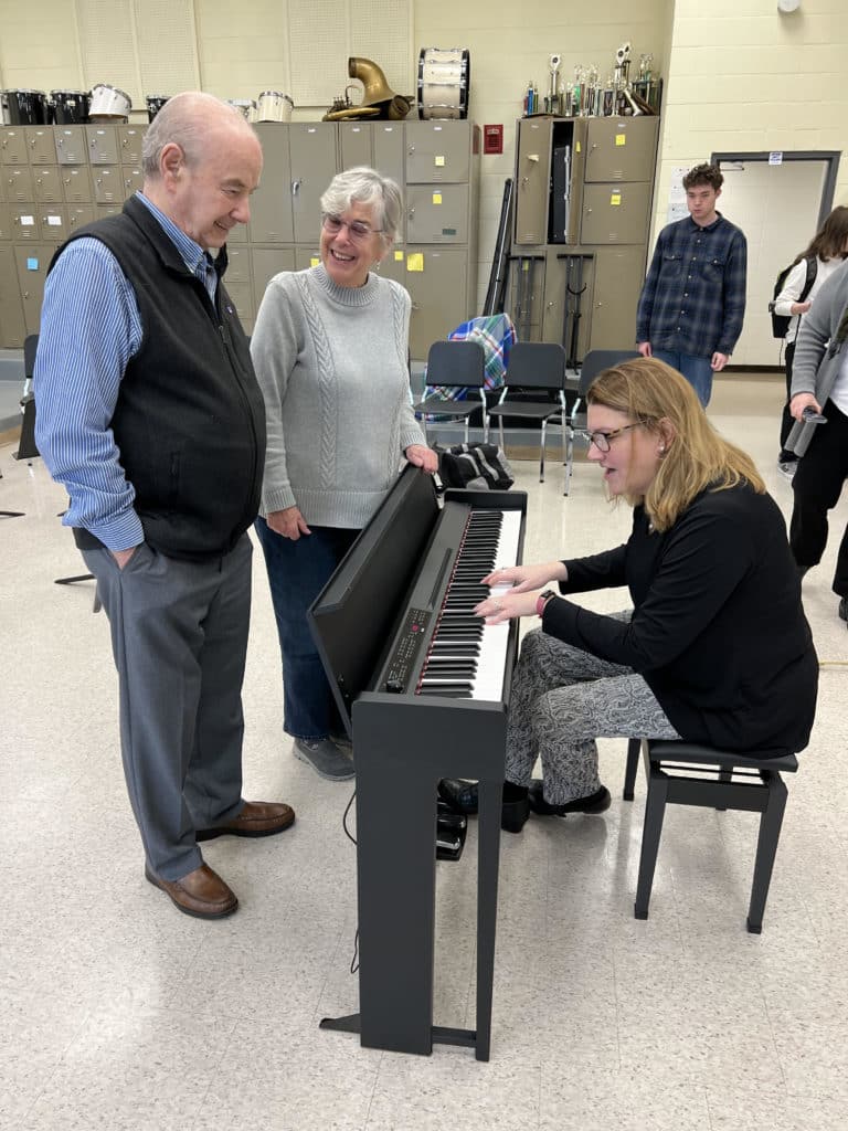 Bourne High School music teacher Lisa Fournier tests the piano donated to the school by Bob and Barbara Pacheco (standing). (Photo courtesy Bourne Public Schools)